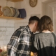 Couple standing in kitchen looking at something in their hand, facing away from camera