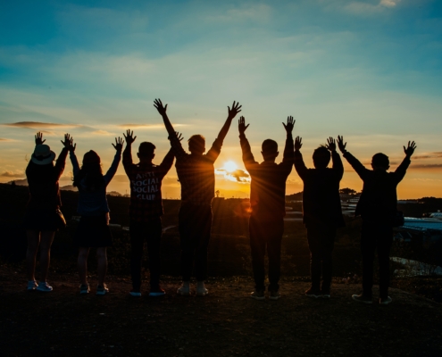 6 people waving their hands up at a sunset