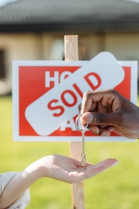 Someone giving a house key to someone behind 'house sold' sign